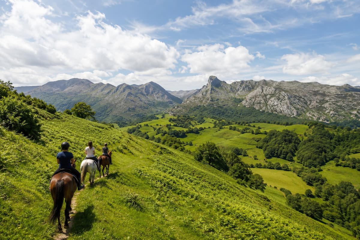 Jinetes avanzando por una ladera verde con vistas panorámicas a las montañas de Asturias