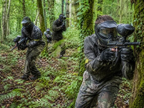 Jugadores de paintball avanzando entre árboles y helechos en un bosque asturiano.