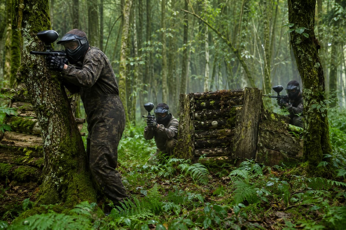 Grupo de jugadores de paintball cubriéndose tras obstáculos de madera en un bosque húmedo de Asturias.