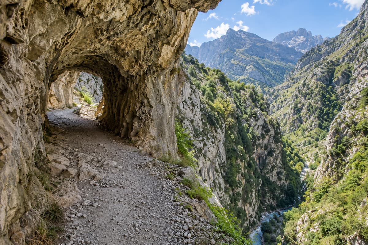 Túnel excavado en la roca en la Ruta del Cares con vistas al desfiladero y las montañas.